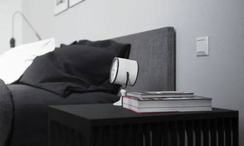 Modern bedside vignette with black furniture, alarm clock, and design books