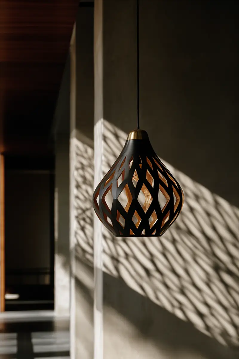 Black and brass geometric pendant light casting dramatic diamond shadow patterns on minimalist white wall
