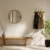 Bright minimalist entryway with wooden bench, round mirror, wall hooks, and potted plants in natural light