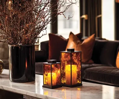Sophisticated living room with subtile luxury Halloween decorations featuring amber crystal hurricane lanterns on marble table, bronze sculptural branches in black vases, cognac leather pillows on charcoal sofa, warm atmospheric lighting