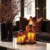 Sophisticated living room with subtile luxury Halloween decorations featuring amber crystal hurricane lanterns on marble table, bronze sculptural branches in black vases, cognac leather pillows on charcoal sofa, warm atmospheric lighting