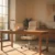 Warm minimalist home office with oak wood desk, ergonomic swivel chair, and floor-to-ceiling windows providing natural light